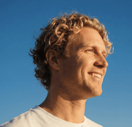 A smiling man with blond curly hair against a blue sky