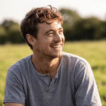 A smiling man with curly hair in a sunlit field