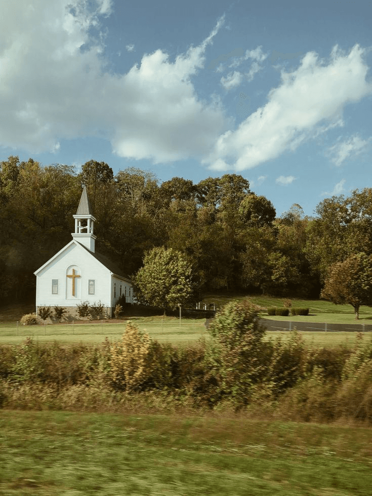 A small white country church with a steeple on a sunlit hillside